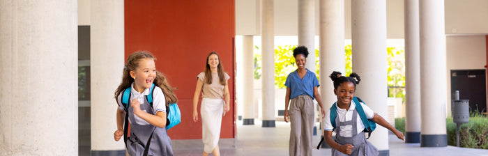 image shows children in school uniforms running through a hallway, with their mothers behind them