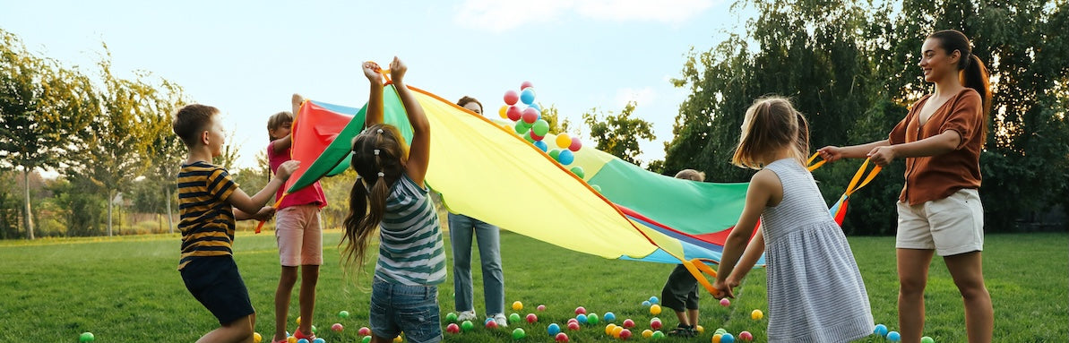 children are playing with multicolored balls and a large parachute in a grassy field