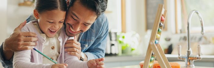 a dad and a daughter are smiling as they work together on an activity
